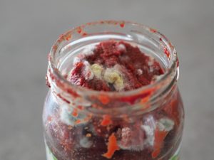 A close-up of mouldy tomato paste in a glass jar, demonstrating how cool room temperature fluctuations can spoil stored food.
