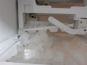A home refrigerator ice maker struggling with slow ice production, with large uneven cubes accumulating in the ice bin.