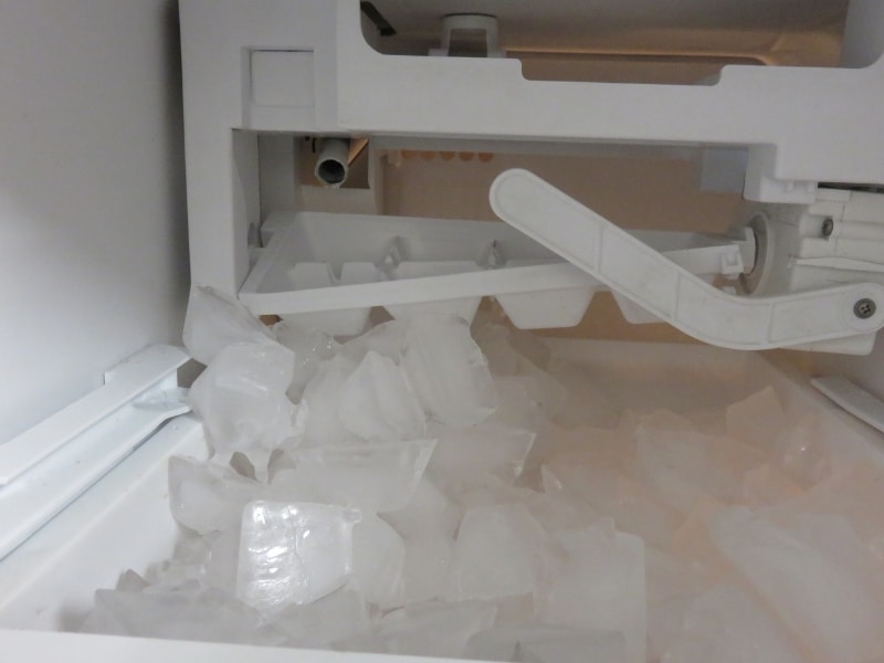 A home refrigerator ice maker struggling with slow ice production, with large uneven cubes accumulating in the ice bin.