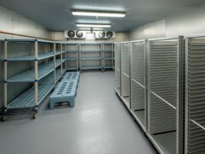 Empty cool room with metal racks and industrial shelving. Cool room repair signs include frost buildup and inefficient cooling.