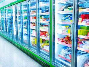 Stocked commercial freezer not cooling efficiently, displaying frozen goods behind glass doors with bright lighting and visible condensation.