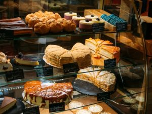 A glass display case shows a variety of cakes; poor cake display maintenance is evident in the disorganised arrangement.