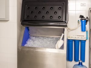 A commercial ice machine, the age of ice machine unknown, is full of ice with a scoop inside.