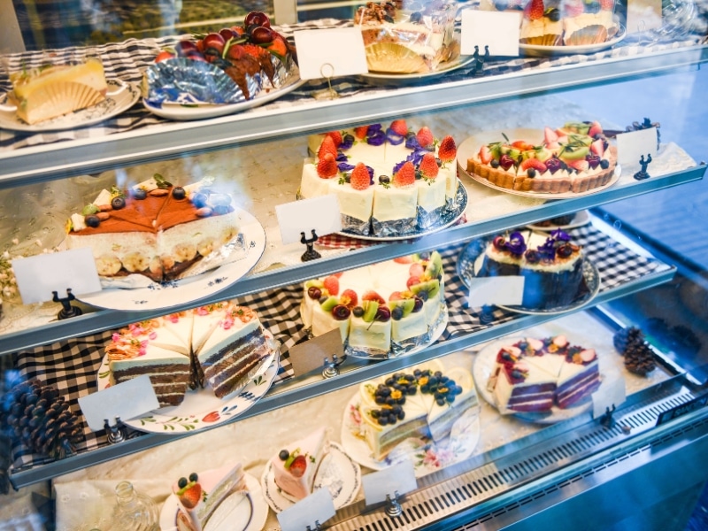 A refrigerated cake display fridge with multiple shelves showcasing various colorful cakes and desserts, maintaining the correct temperature.