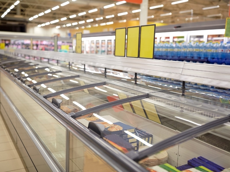 Horizontal chest freezers in a supermarket with visible frozen foods, possibly pointing to a freezer making loud noise.