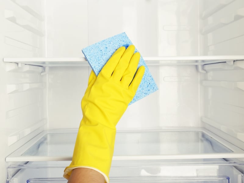 Person cleaning refrigerator shelves wearing yellow gloves for restaurant freezer repair hygiene.