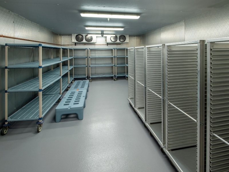 Cool room cleaning with empty metal racks and plastic shelving ready for hygienic storage preparation. 